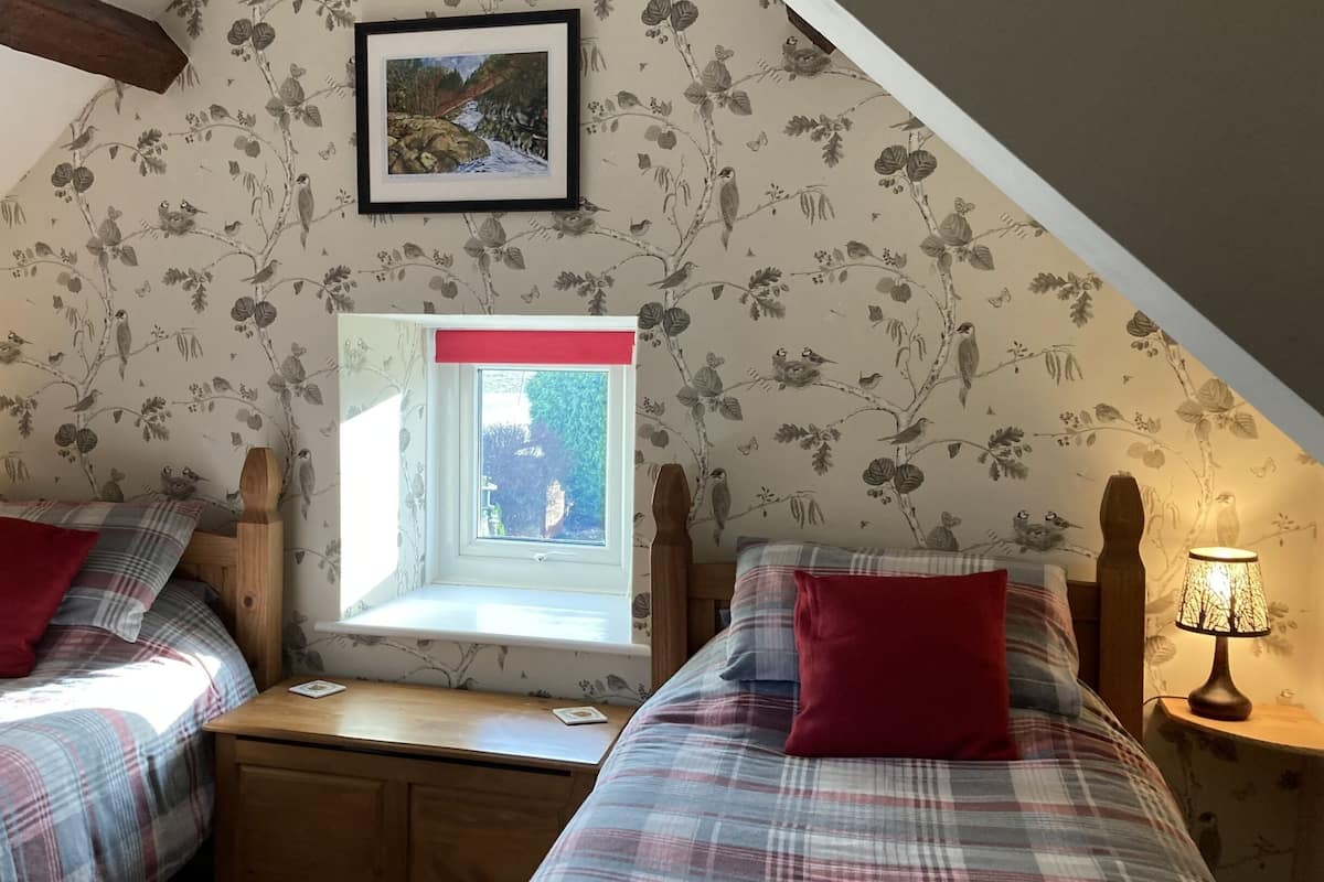 Une chambre avec deux lits, une fenêtre et un mur orné d’un motif d’oiseaux.