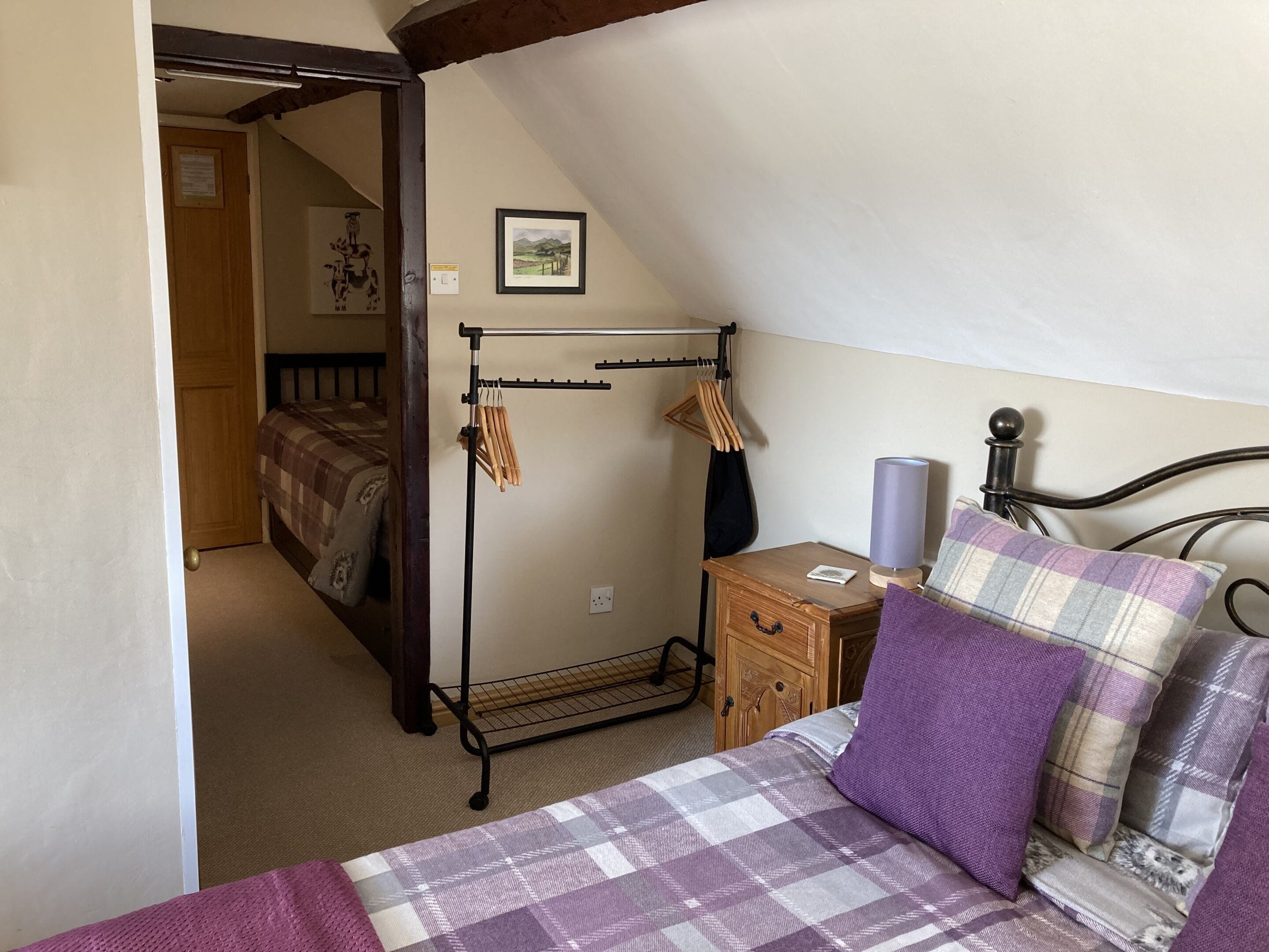 Um quarto com uma cama, uma mesinha de cabeceira de madeira, um cabideiro e um quadro na parede.