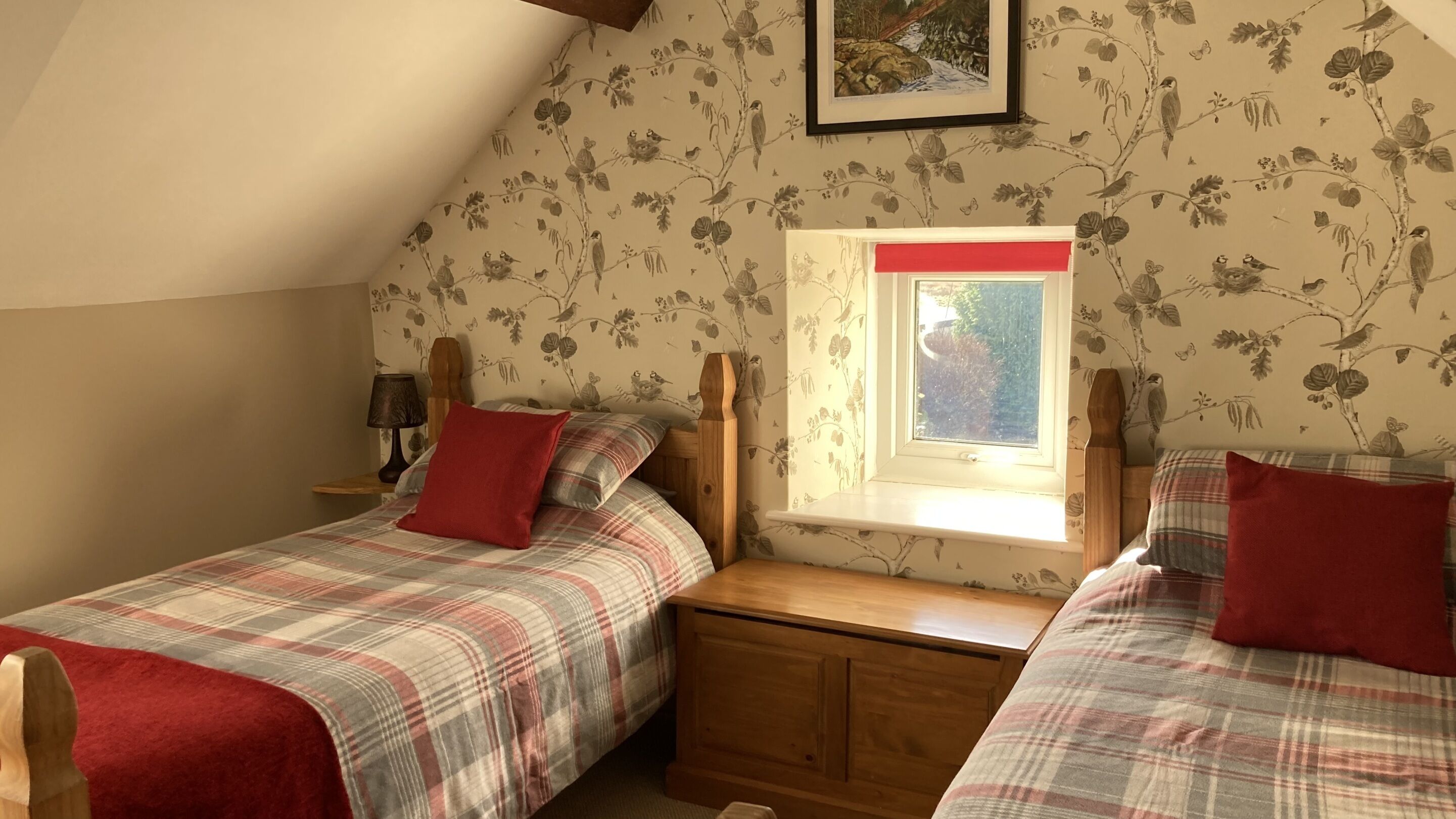 A bedroom with two beds, a window, and floral wallpaper.