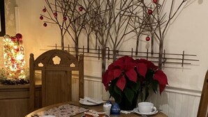 Une table de salle à manger ronde en bois, entourée de chaises blanches, agrémentée d’un centre de table composé de poinsettias rouges et d’une branche décorative fixée au mur.