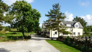 Une maison avec une allée en gravier, entourée de verdure et d’un mur de pierres.