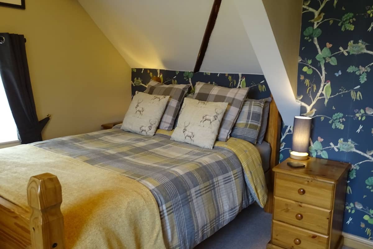 Une chambre à coucher avec un lit, une table de chevet, une lampe et un mur décoré d’un motif représentant un arbre et des oiseaux.