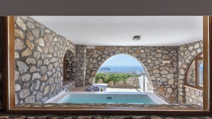 Une pièce aux murs de pierre offrant une vue sur une piscine et la mer.