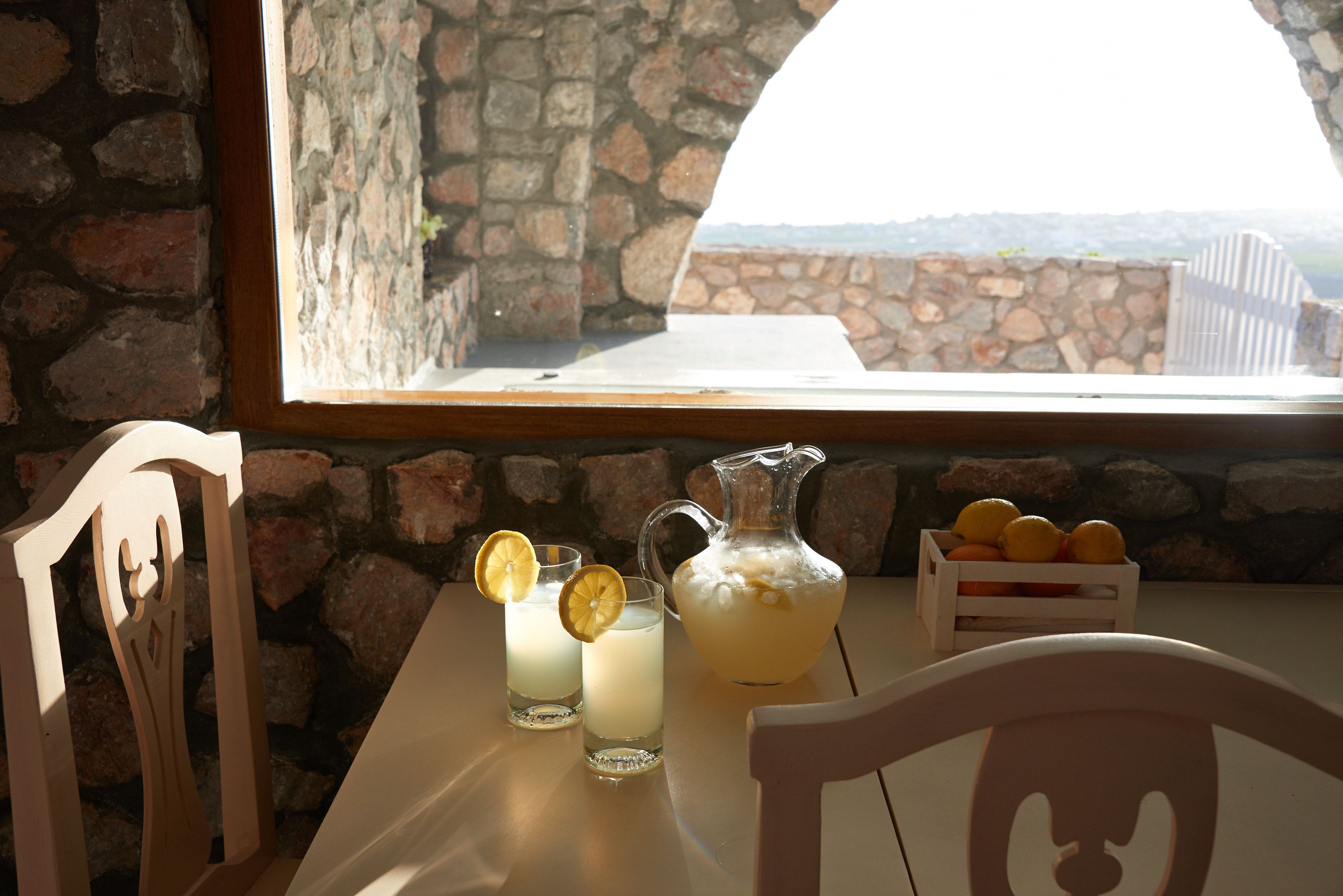 Une table avec deux verres contenant une boisson de couleur claire, une carafe et une caisse de citrons.