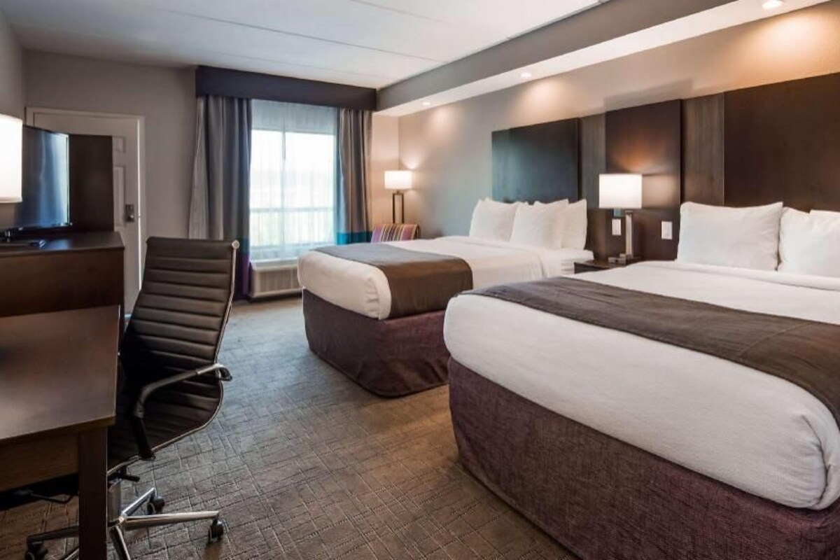 A hotel room with two beds, a desk, a chair, and a television.