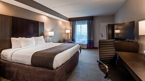 Een hotelkamer met een groot bed, een bureau met een flatscreen televisie, een stoel en een raam met gordijnen.