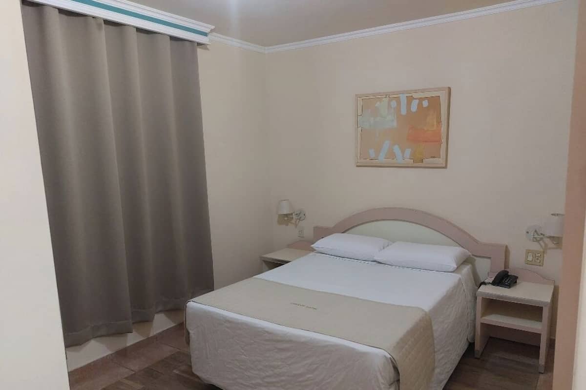 Habitación de hotel ordenada con una cama, mesitas de noche, una lámpara y un cuadro en la pared.