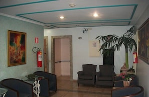 A lobby with a reception desk, two armchairs, a large potted plant, and a fire extinguisher on the wall. - Prince Hotel (Ribeirão Preto)