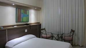 Una habitación de hotel con una cama, un escritorio con una silla, un teléfono y un cuadro en la pared.