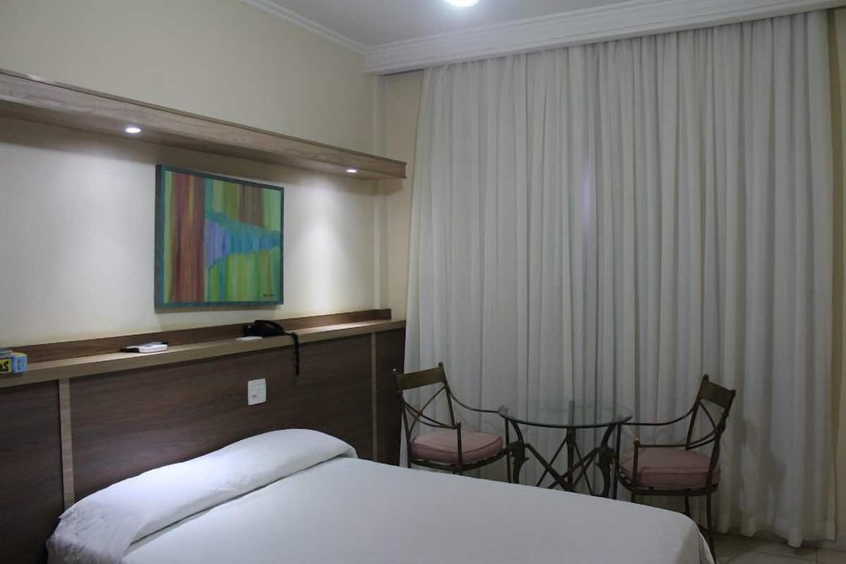 Una habitación de hotel con una cama, un escritorio con una silla, un teléfono y un cuadro en la pared.