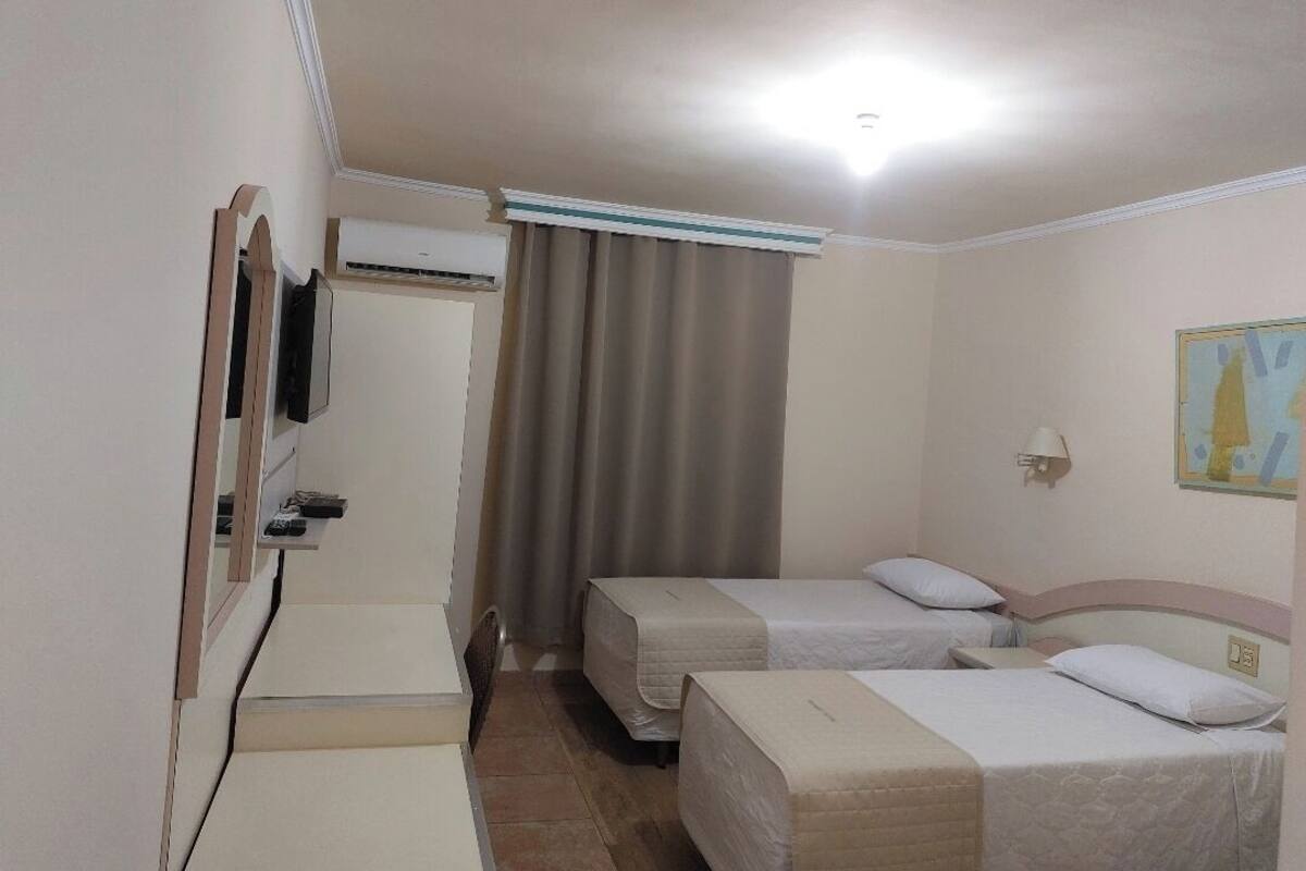 Habitación de hotel con dos camas, un escritorio, un televisor y una ventana con cortinas.