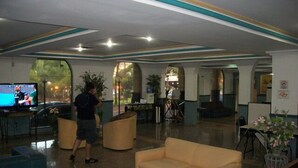 Un hall con mostrador de recepción, zona de estar y un televisor mostrando un evento deportivo.