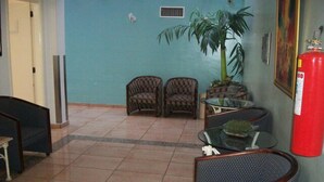 Un hall con dos sillones de mimbre, una mesa de vidrio, una planta en maceta y un extintor.