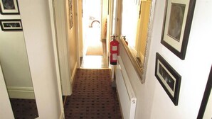 A narrow hallway with patterned carpet, a fire extinguisher mounted on the wall, and framed pictures on the walls.