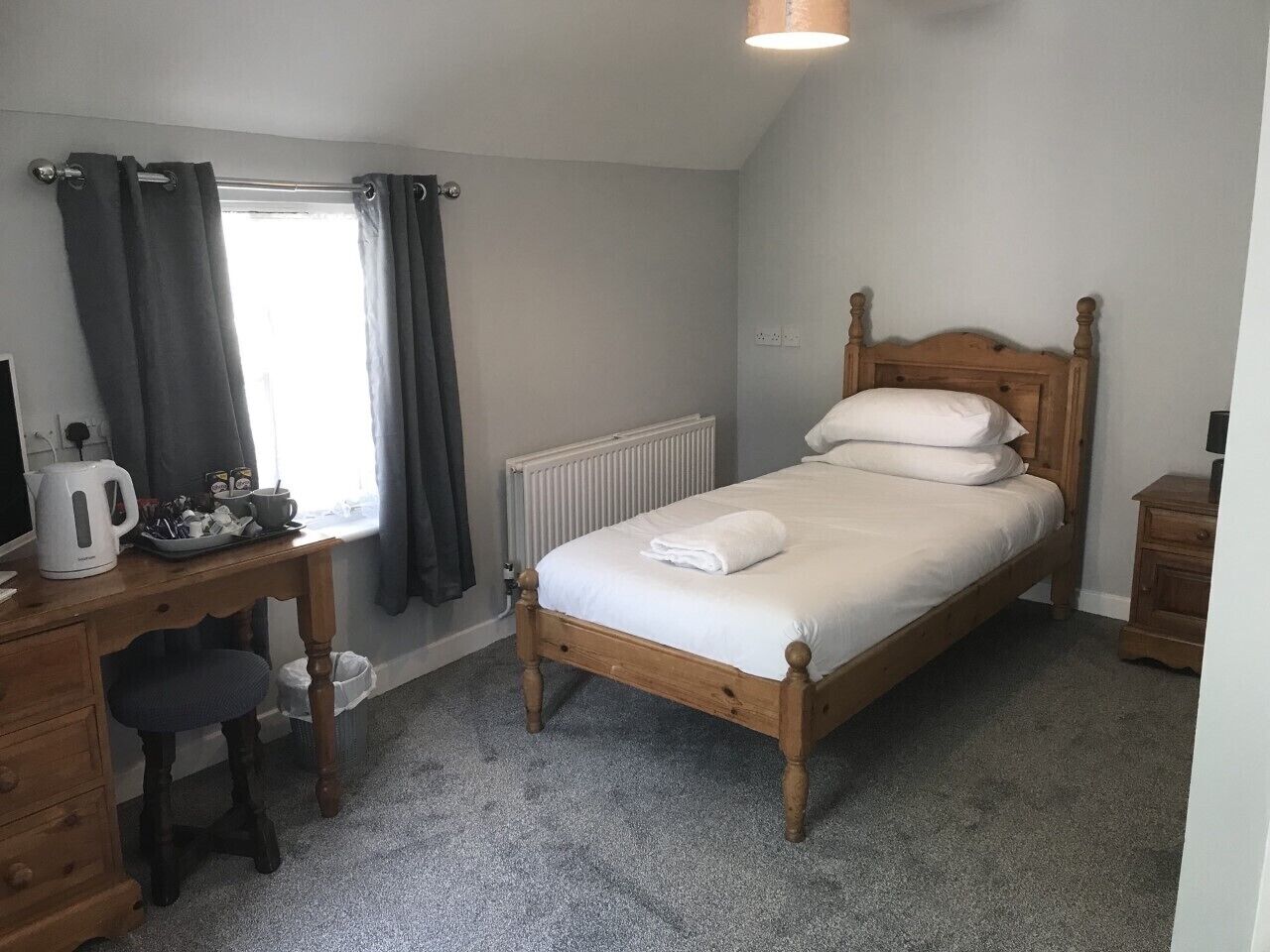 A bedroom with a wooden bed, a desk with a kettle, and a radiator.