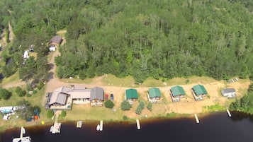 An aerial view of a lakeside property with multiple cabins, a main lodge, and several boats docked at the pier.