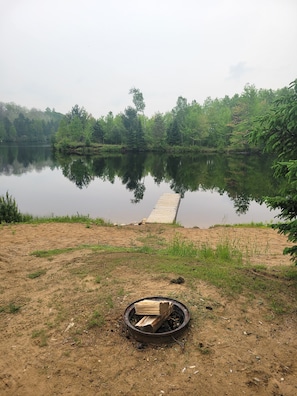 Une scène au bord d’un lac, avec une jetée s’avançant dans l’eau, le tout entouré d’une végétation luxuriante.