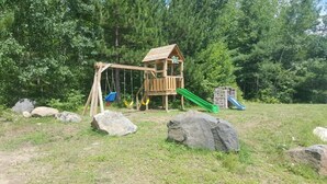 A wooden playground with swings, a slide, and a small house structure. - All Star Resort (South Algonquin)