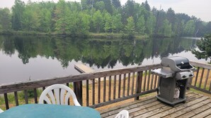 A wooden deck with a grill and chairs overlooking a calm lake. - All Star Resort (South Algonquin)