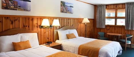 A hotel room with two beds, a wooden headboard, a small table, two chairs, and a window with curtains.