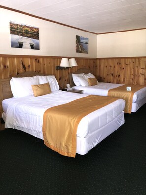 A hotel room with two beds, wooden headboard, a nightstand, a lamp, and two wall-mounted paintings. - Wakita Motel (Queensbury)
