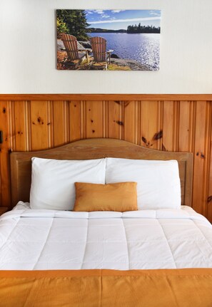 A bed with a wooden headboard, white bedding, and a single brown pillow. - Wakita Motel (Queensbury)