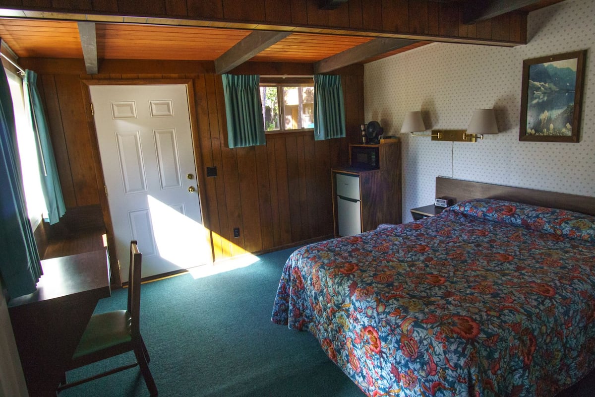 A bedroom with a bed, a desk, a chair, a dresser, and a door.