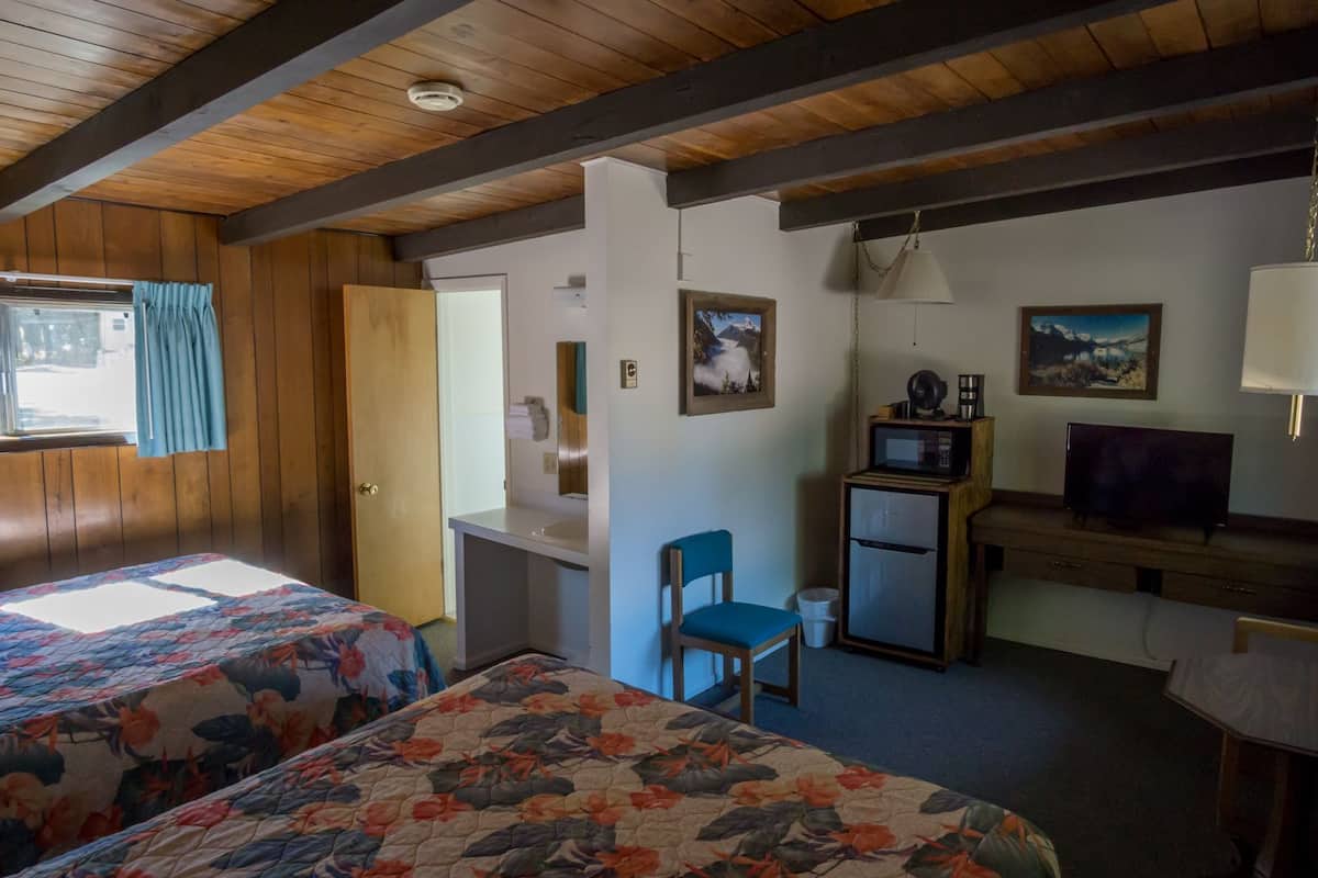 A room with two beds, a desk, a chair, a television, and a microwave.