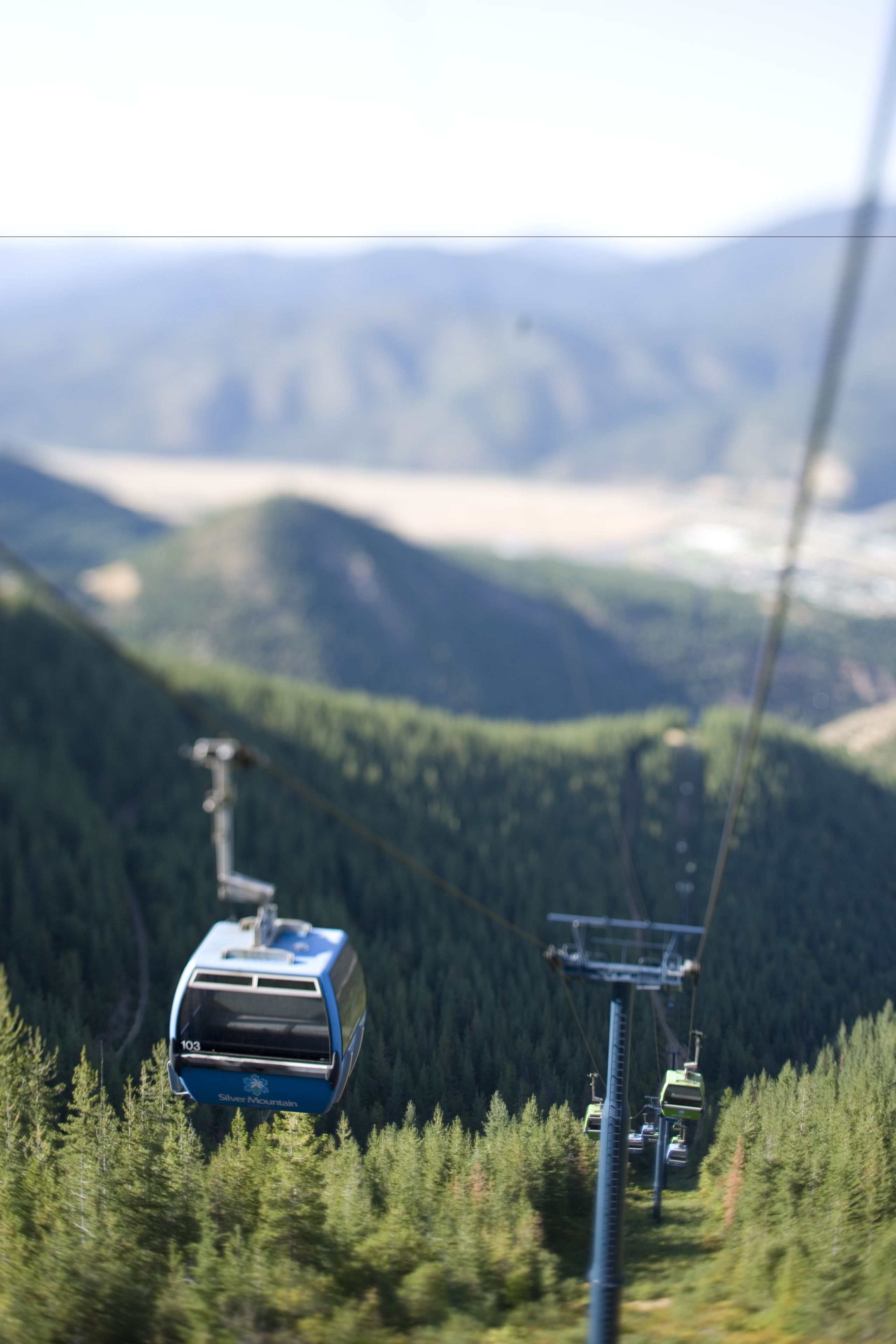 A cable car moving along a mountain cable system with a forested valley in the background.
