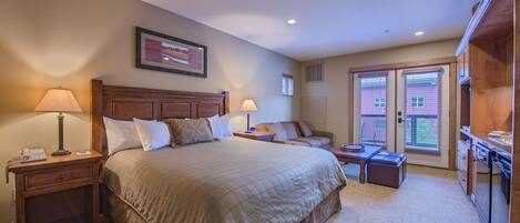 A bedroom with a large bed, two bedside tables with lamps, a nightstand, a wooden bench, and a desk with a chair.