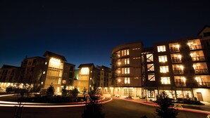 A multi-story hotel with illuminated windows and balconies, a central courtyard, and a roundabout with light trails.