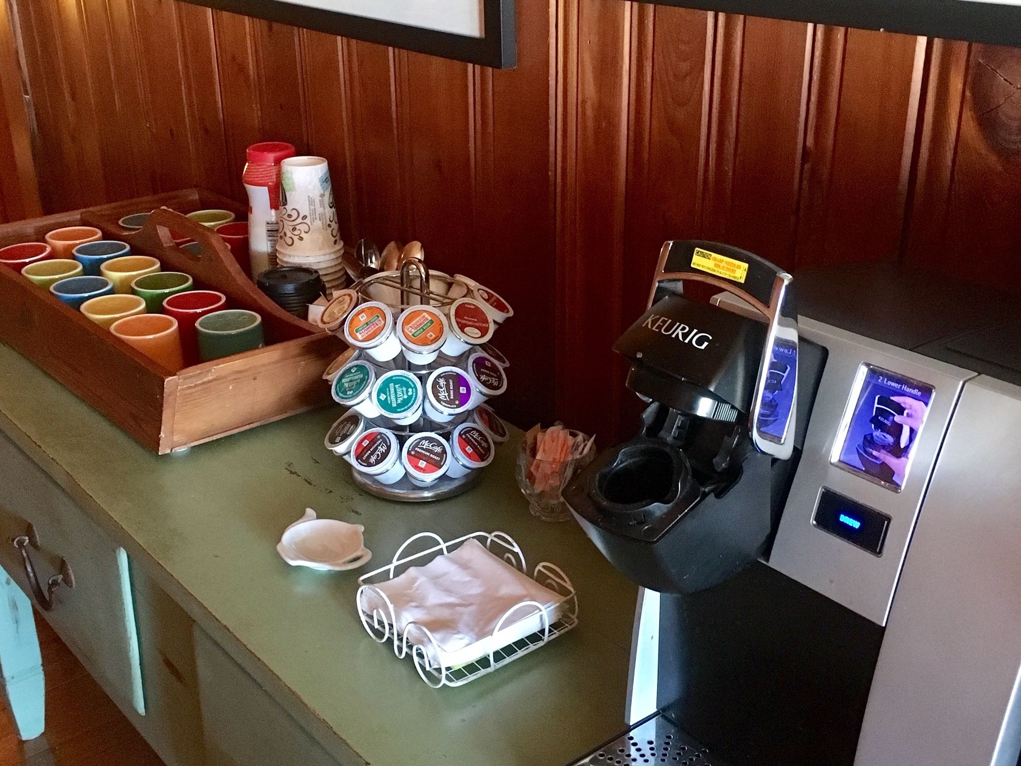 A coffee machine with multiple coffee pods, a tray of colorful cups, and a white basket on a counter.
