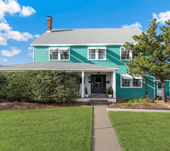 A two-story house with a green exterior, white trim, and a grey roof.
