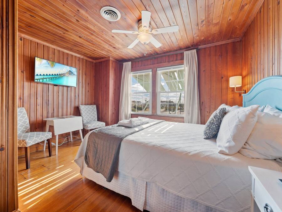 A wooden-paneled room with a bed, a desk, a chair, a television, and a window.