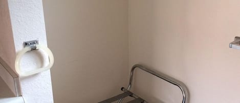 A small bathroom with a metal drying rack, a trash bin, and a wooden hanger on the wall.