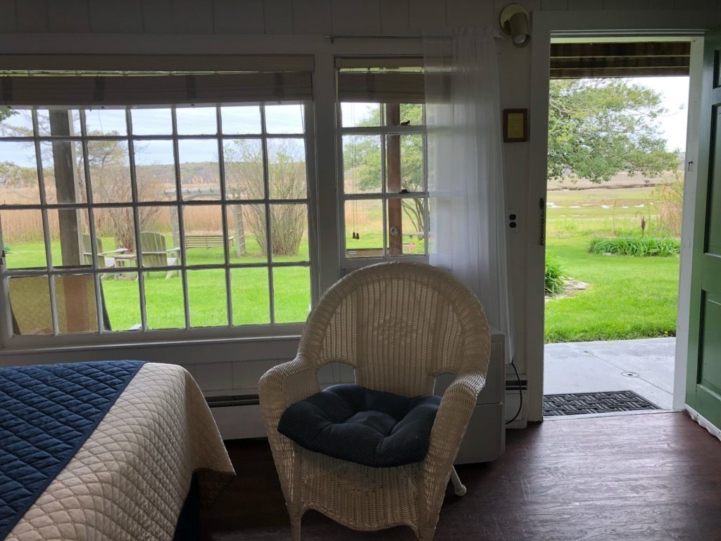 Una habitación con una cama, una silla de mimbre con cojín y una puerta que da a un jardín.
