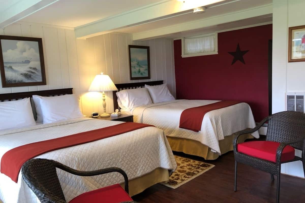 A hotel room with two beds, a nightstand, a lamp, a chair, and a star decoration on the wall.