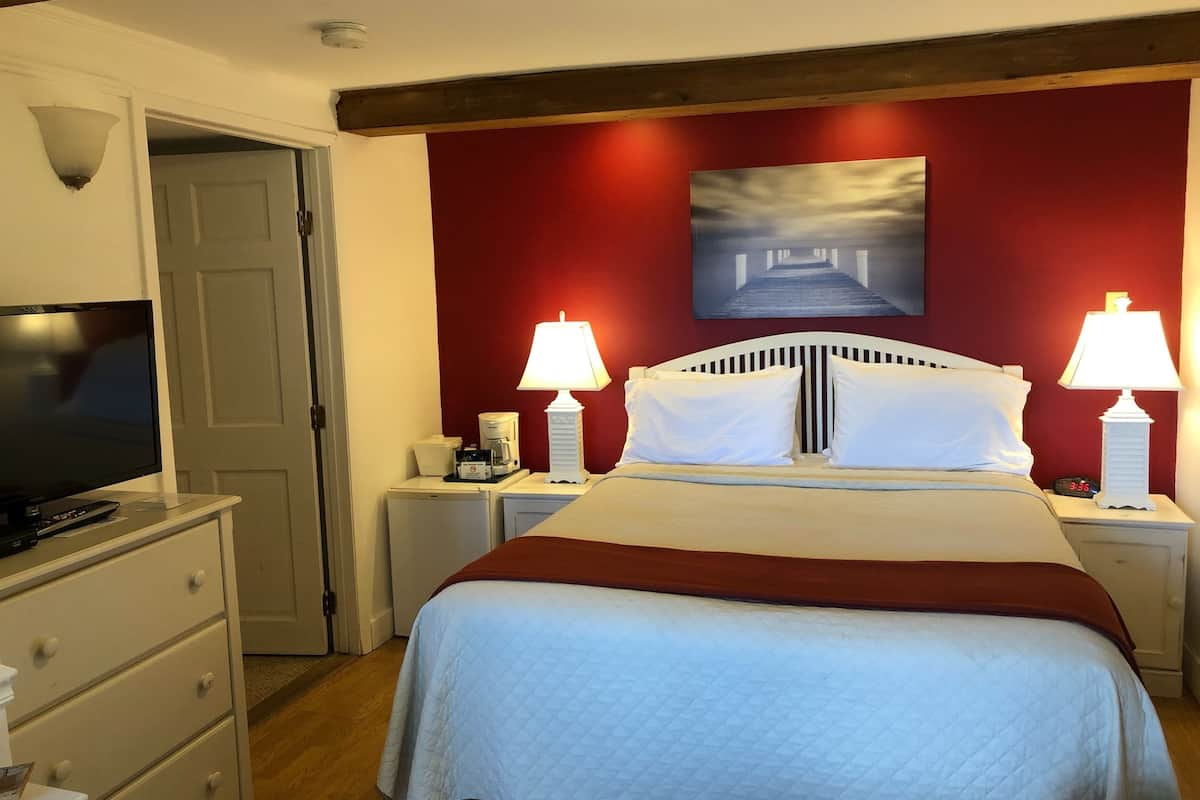 A hotel room with a bed, two bedside lamps, a TV, a coffee maker, and a painting on the wall.