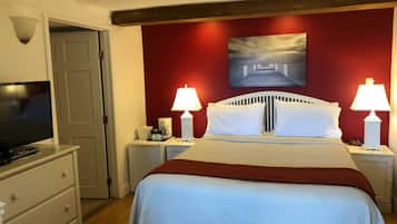 Une chambre d’hôtel avec un lit, deux lampes de chevet, une télévision, une machine à café et un tableau au mur.