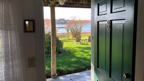A green door leading to a covered porch with a view of a lake and autumn foliage. - Spring Garden Inn (East Sandwich)