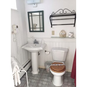 A bathroom with a white sink, a toilet with a wooden seat, a mirror with a green frame, and a black shelf above the toilet.