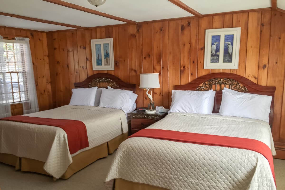 A room with two beds, wooden walls, and framed pictures on the wall.