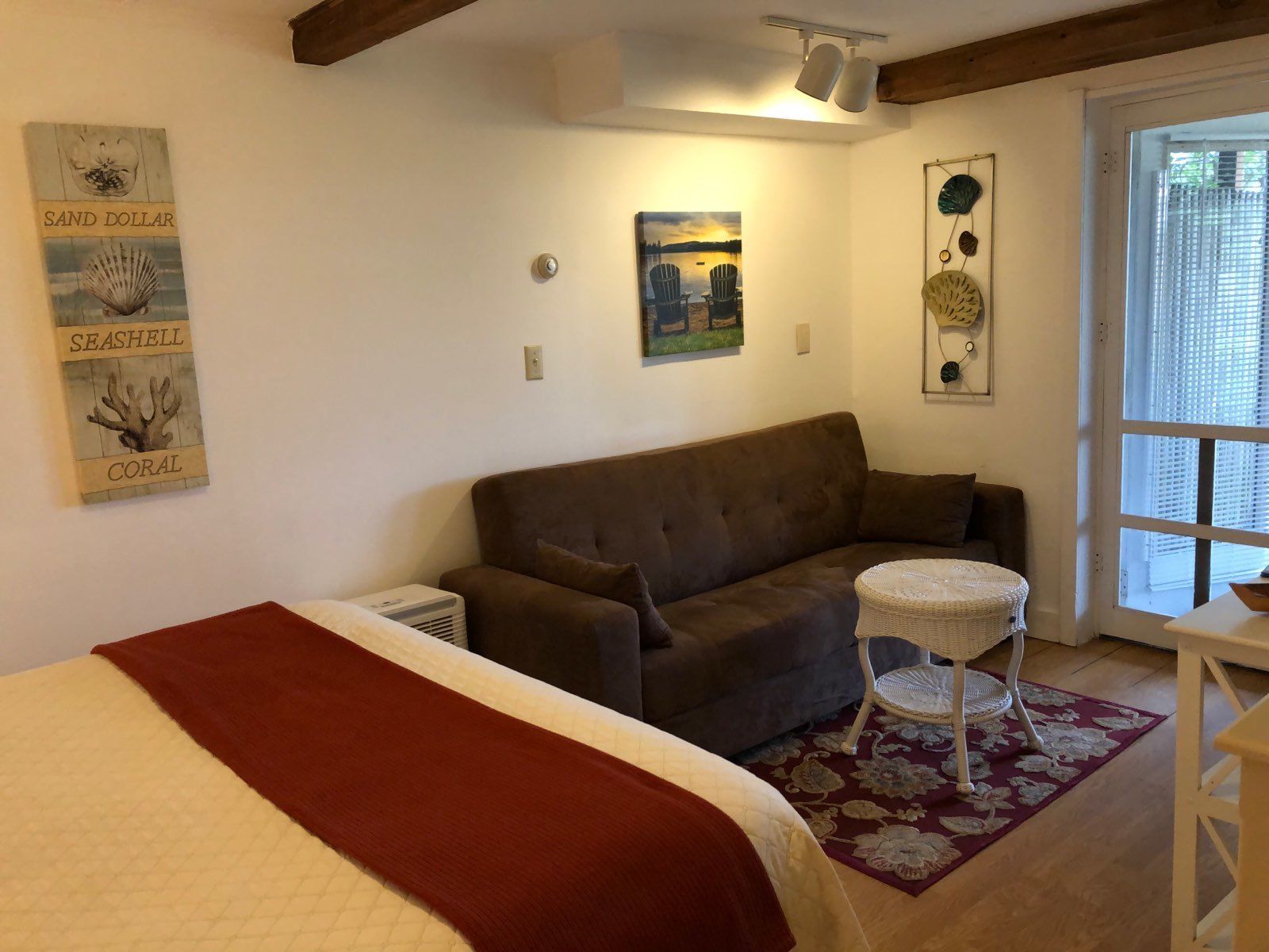 Une pièce confortable avec un lit, un canapé marron, une petite table ronde et une fenêtre avec des stores.