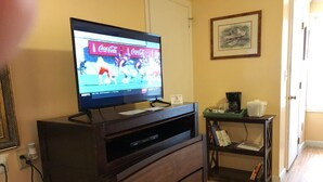 A living room with a flat-screen TV on a wooden stand, a coffee machine, and a bookshelf. - Spring Garden Inn (East Sandwich)