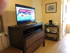 A living room with a flat-screen TV on a wooden stand, a coffee machine, and a bookshelf. - Spring Garden Inn (East Sandwich)