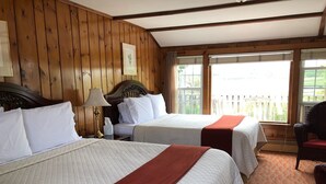 A room with two beds, wooden walls, a window with a view, and a wicker chair. - Spring Garden Inn (East Sandwich)