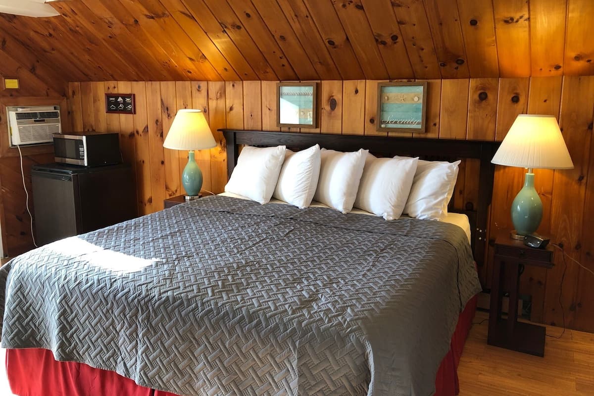A wooden-paneled room with a bed, two bedside lamps, a small table, a microwave, and a television.