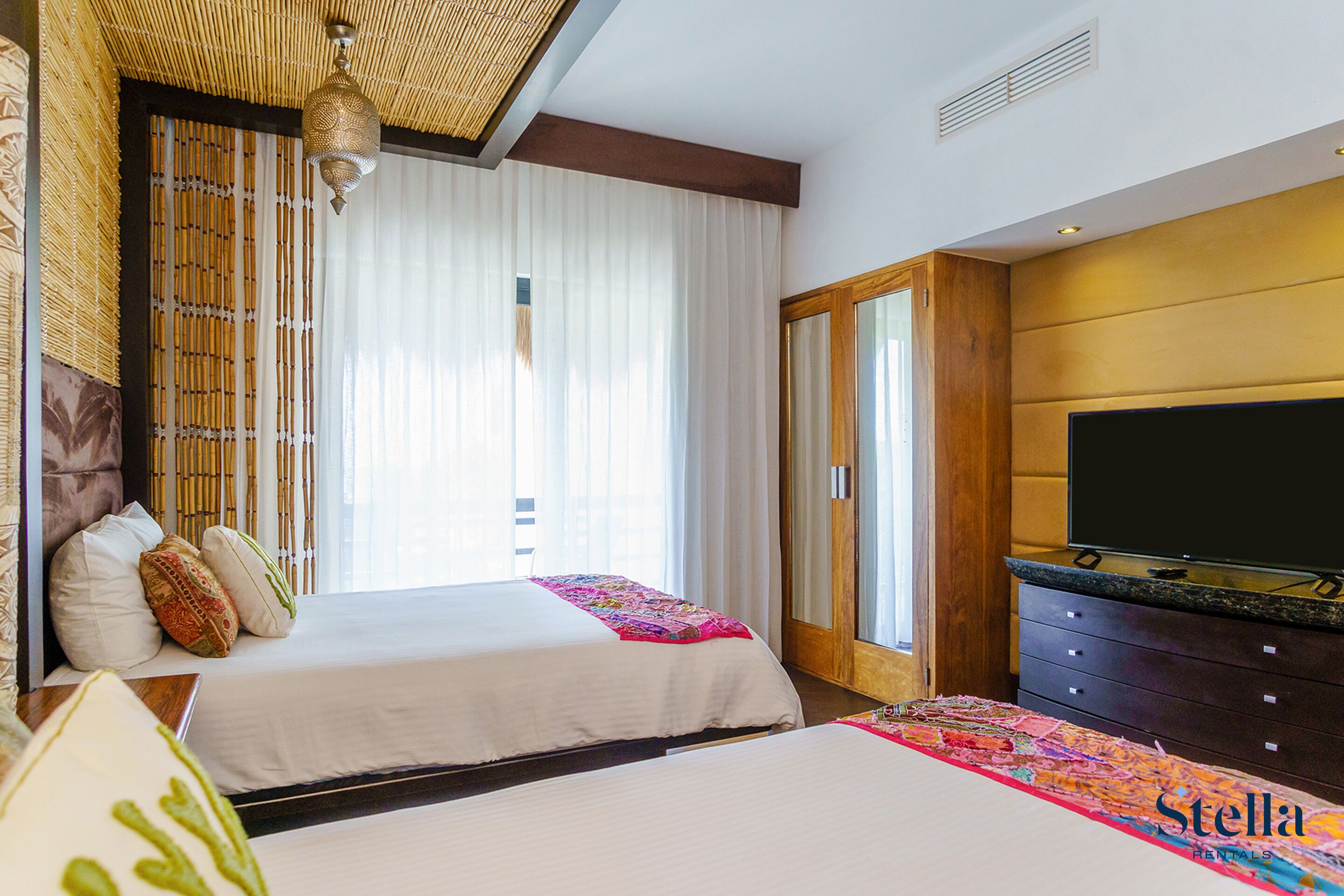 A hotel room with two beds, a television, and a large window with curtains.