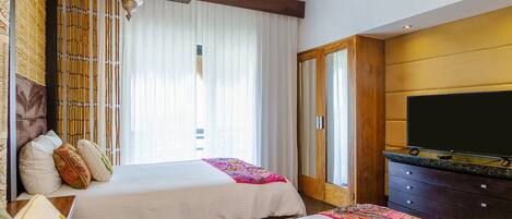 A hotel room with two beds, a television, and a large window with curtains.