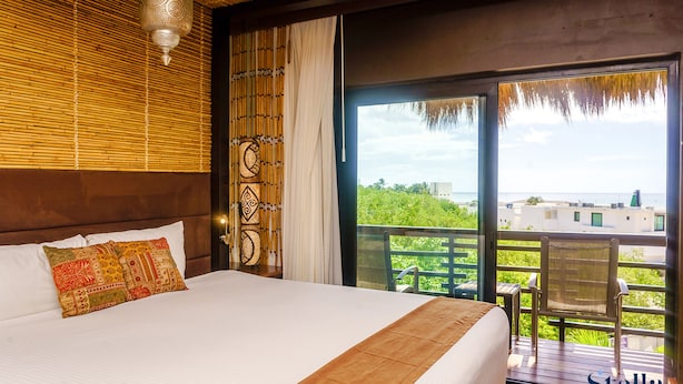 Habitación de hotel con una cama grande, un balcón con vistas y una pared decorativa.